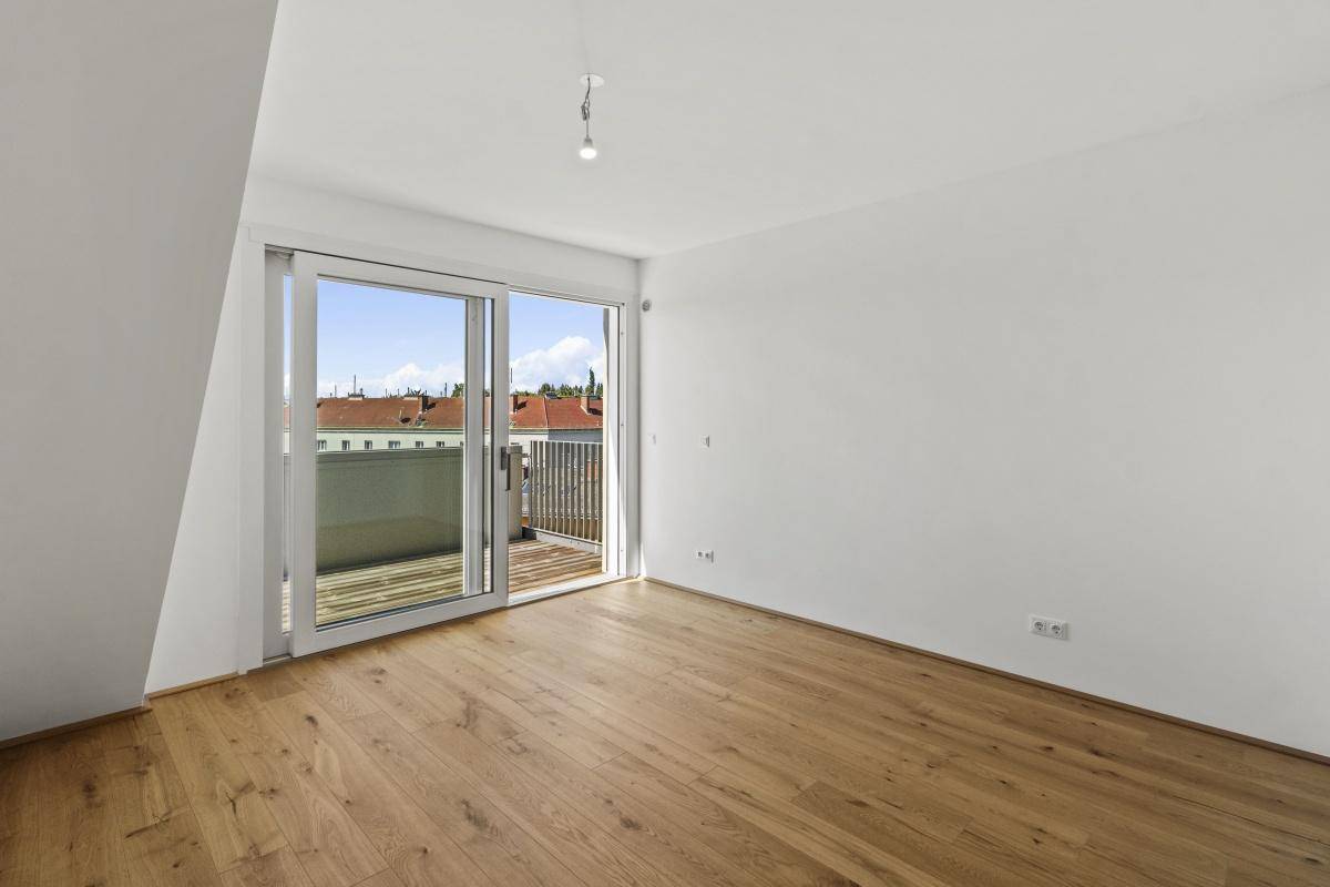Geräumiges Schlafzimmer mit Holzboden und Schiebetür, die auf einen Balkon führt.