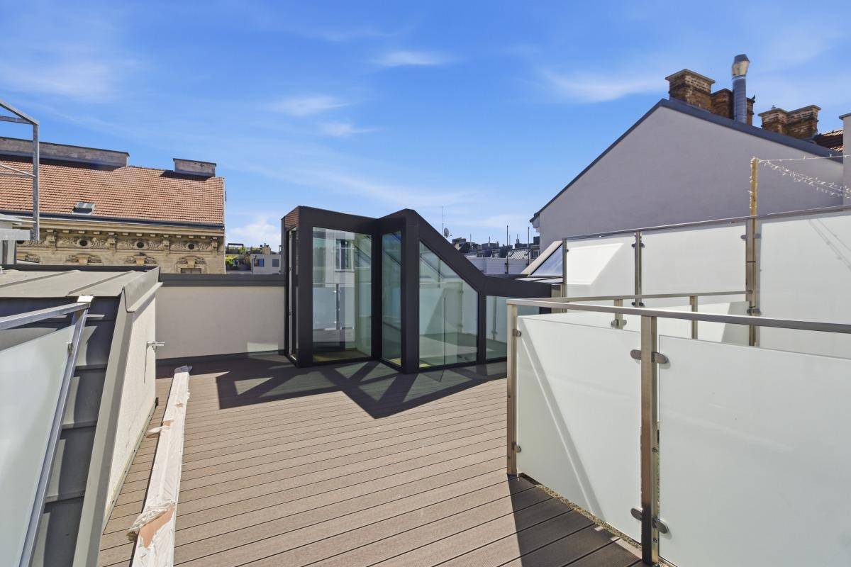 Moderne Dachterrasse mit Glasaufbau und Holzbelag, bietet einen hellen Zugang zum Innenbereich.