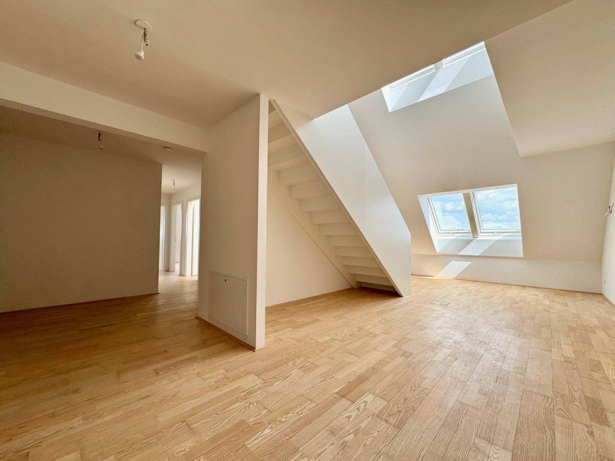 Offener Wohnbereich mit Holzparkettboden, Treppe und mehreren Dachfenstern, die den Raum erhellen.