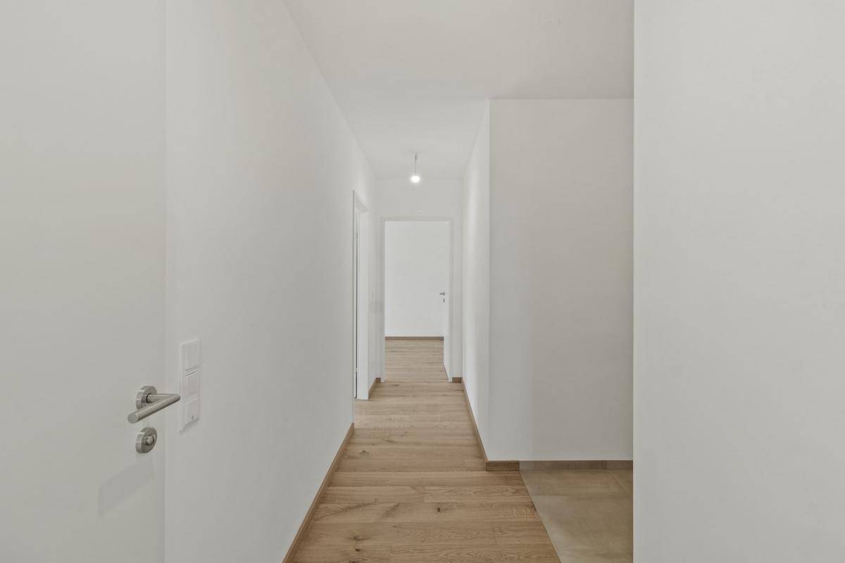 Langer, heller Flur mit Holzboden und weißen Wänden, der zu weiteren Räumen führt.