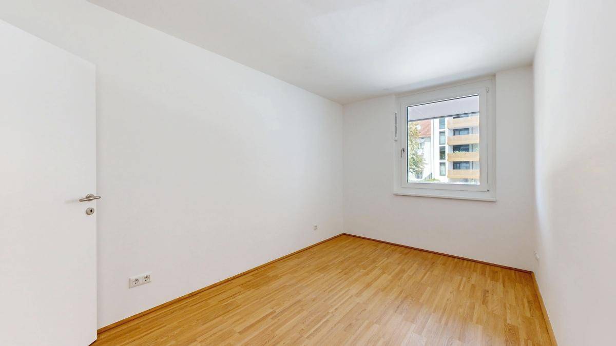 Ruhiges Schlafzimmer mit Parkettboden und großem Fenster für viel Tageslicht.