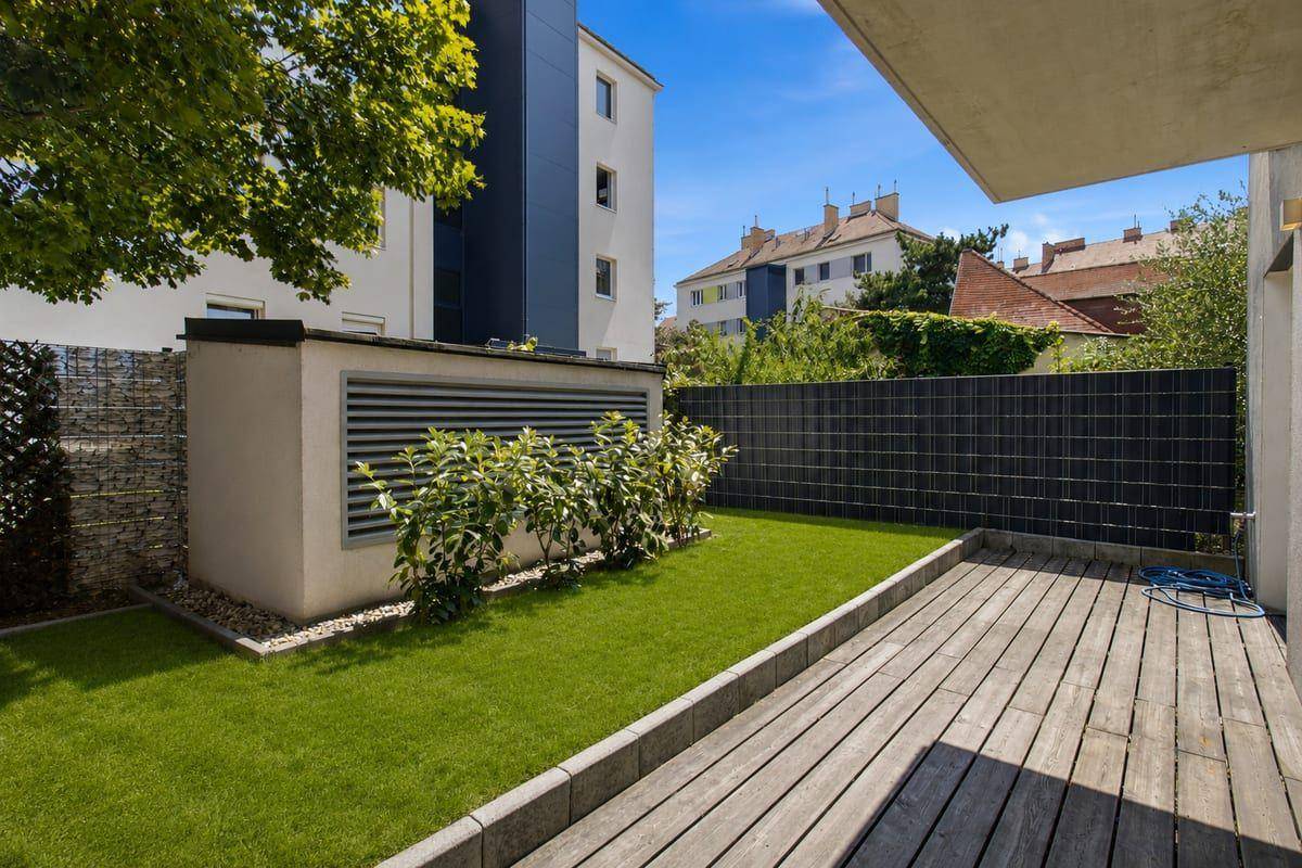 Gepflegter Gartenbereich mit Holzterrasse und Rasenfläche hinter dem Gebäude.