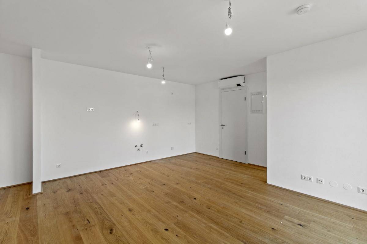 Geräumiger, unmöblierter Wohnraum mit hellen Wänden und modernem Parkettboden.