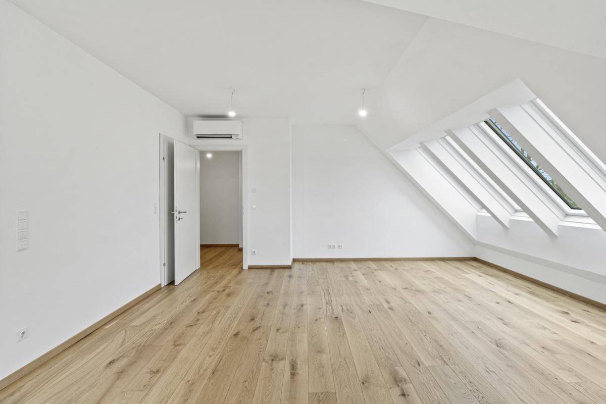 Heller Dachgeschossraum mit Holzboden, Dachfenstern und einer modernen Klimaanlage.