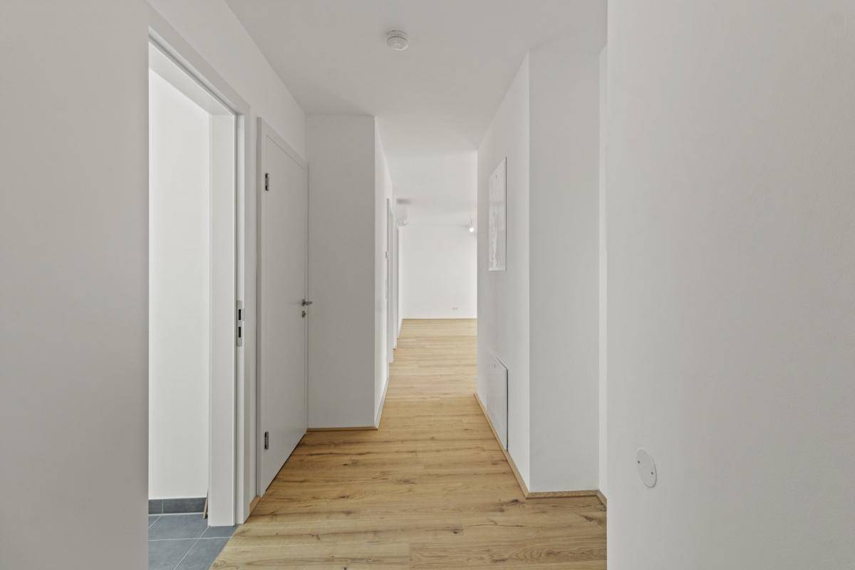 Langer, heller Flur mit Holzboden und weißen Wänden, der zu weiteren Räumen führt.