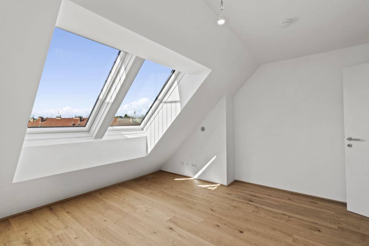 Schlafzimmer mit Holzboden und zwei Dachfenstern, die den Raum mit Licht füllen.