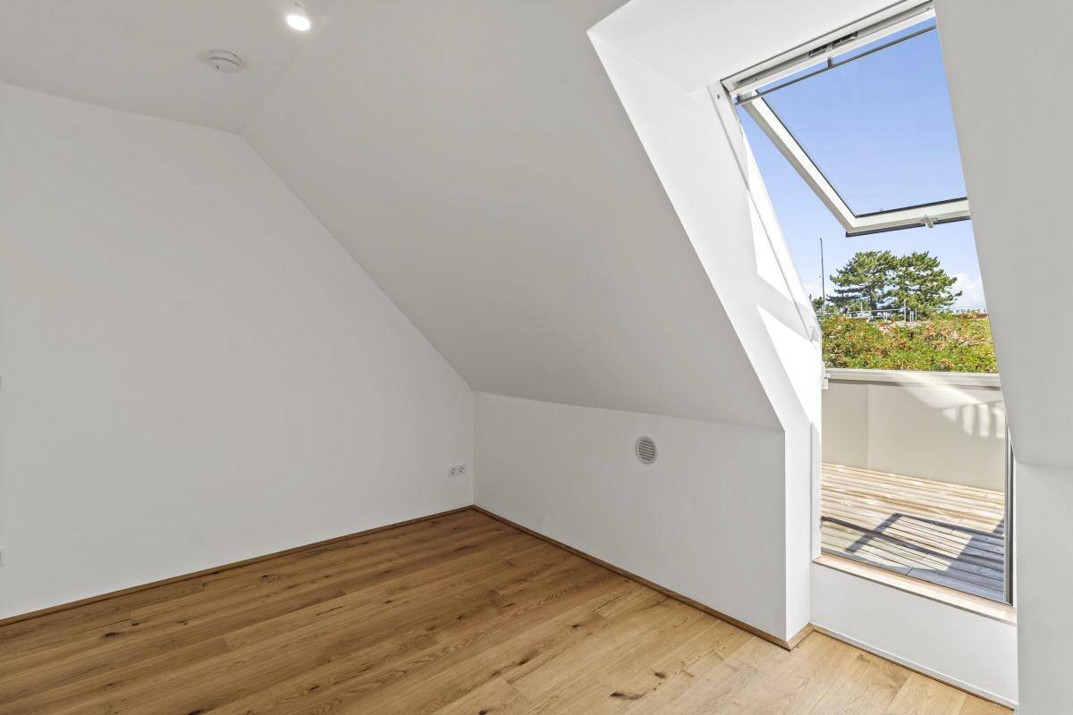 Lichtdurchfluteter Raum im Dachgeschoss mit Holzboden und Zugang zu einem kleinen Balkon.