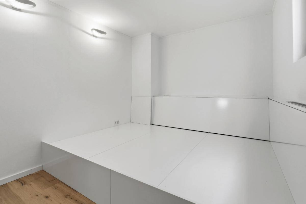 Minimalistisches Schlafzimmer mit weißer Plattform und hellem Holzfußboden.