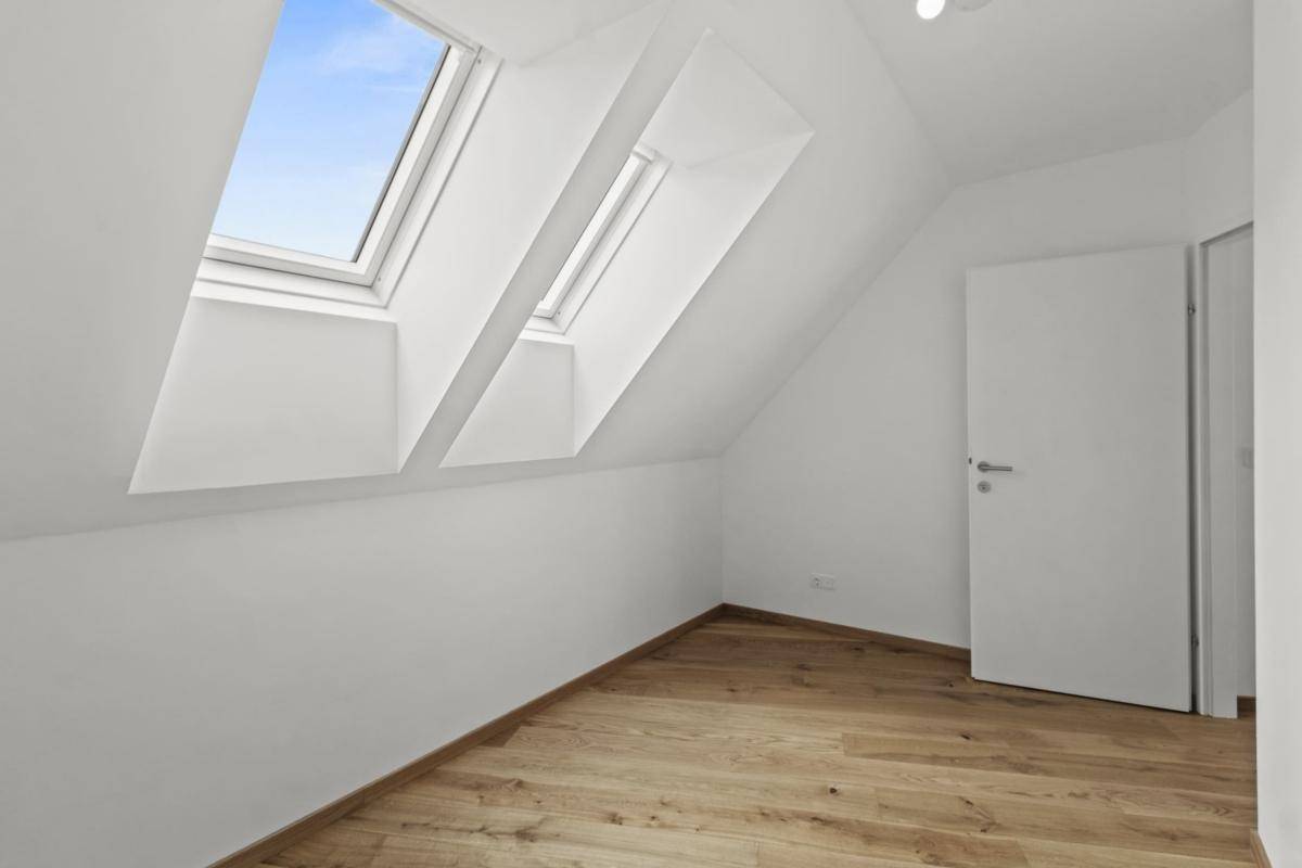 Schlafzimmer mit Holzboden, Dachschräge und zwei Dachfenstern für viel Tageslicht.