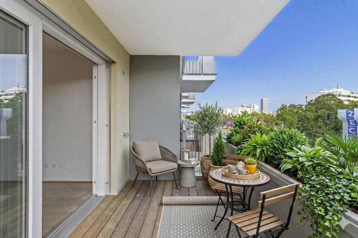 Gemütlicher Balkon mit Holzfußboden, Sitzgelegenheiten und Pflanzen, bietet einen Blick auf die Stadt.