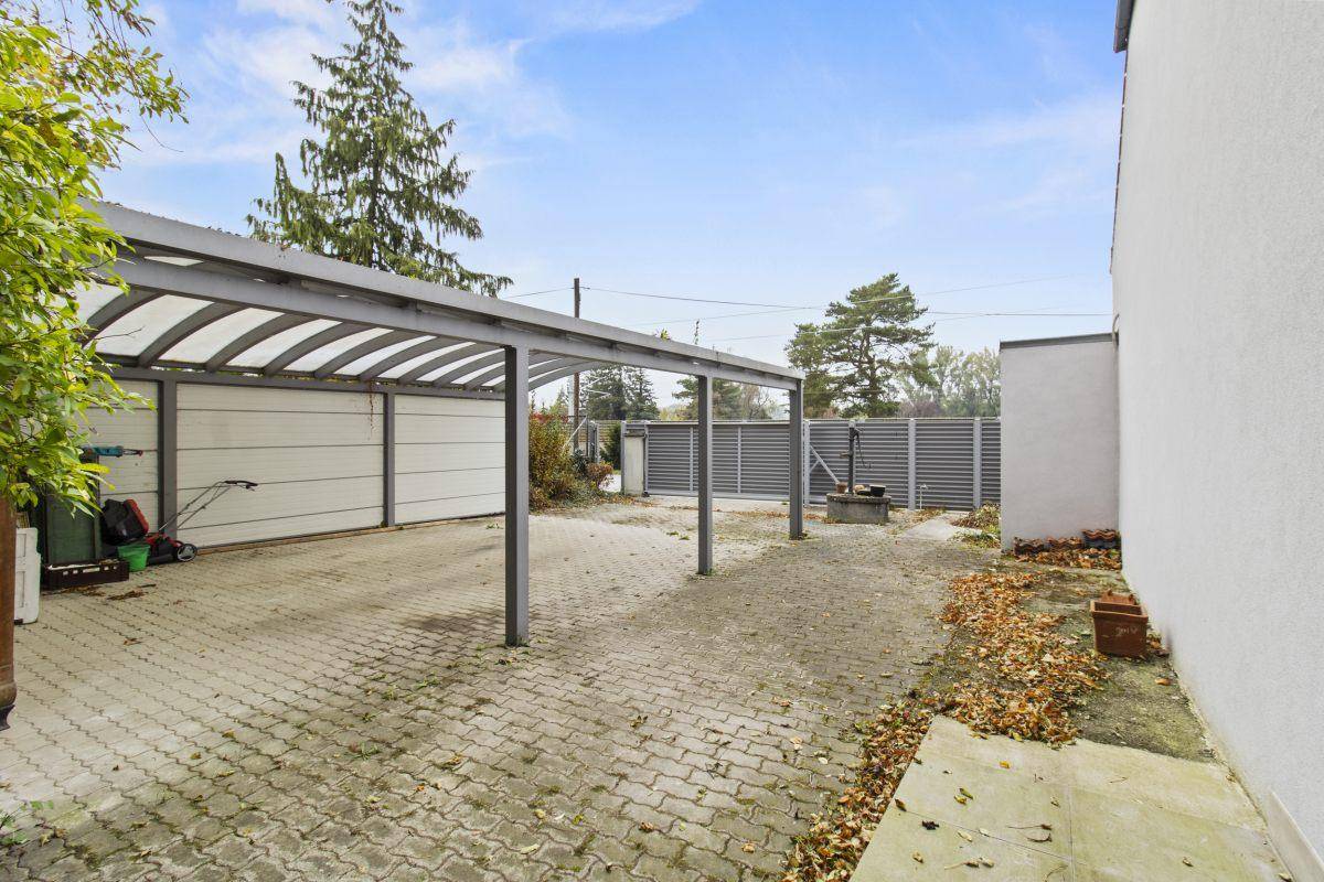 Außenbereich mit einem Carport und einer gepflasterten Auffahrt, umgeben von einem Zaun.