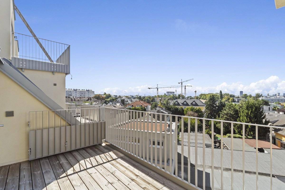 Balkon mit Holzboden und Blick auf die umliegende Bebauung und den Himmel.