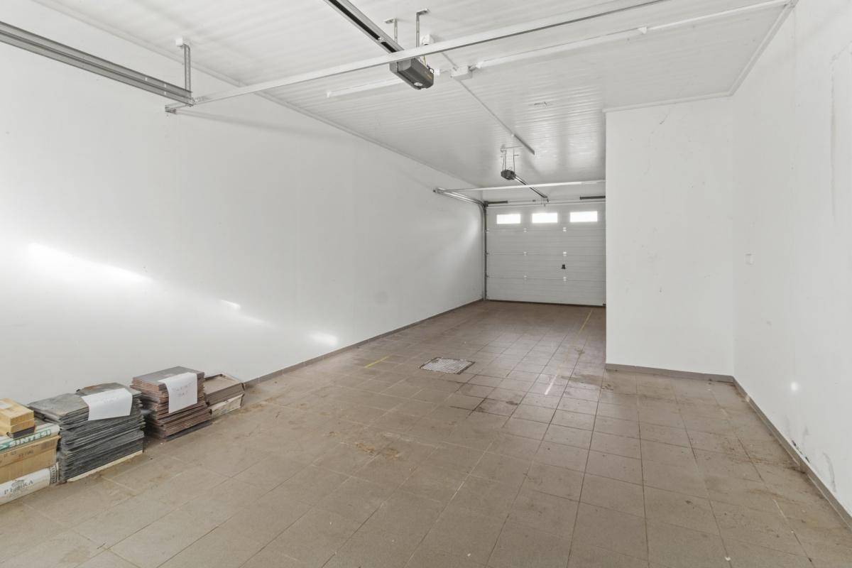 Geräumige Garage mit Fliesenboden und automatischem Garagentor, bereit für Fahrzeuge.