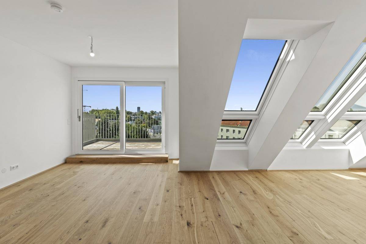 Heller Wohnbereich im Dachgeschoss mit Holzboden, großen Fenstern und Balkonzugang.