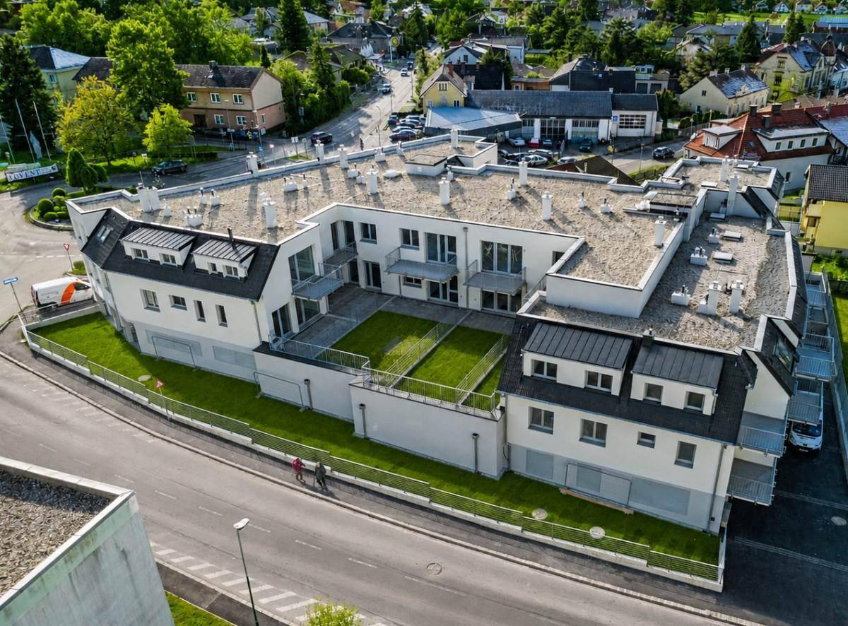 Vogelperspektive eines Neubaus mit Innenhof und begrünten Flächen in einer Wohngegend.