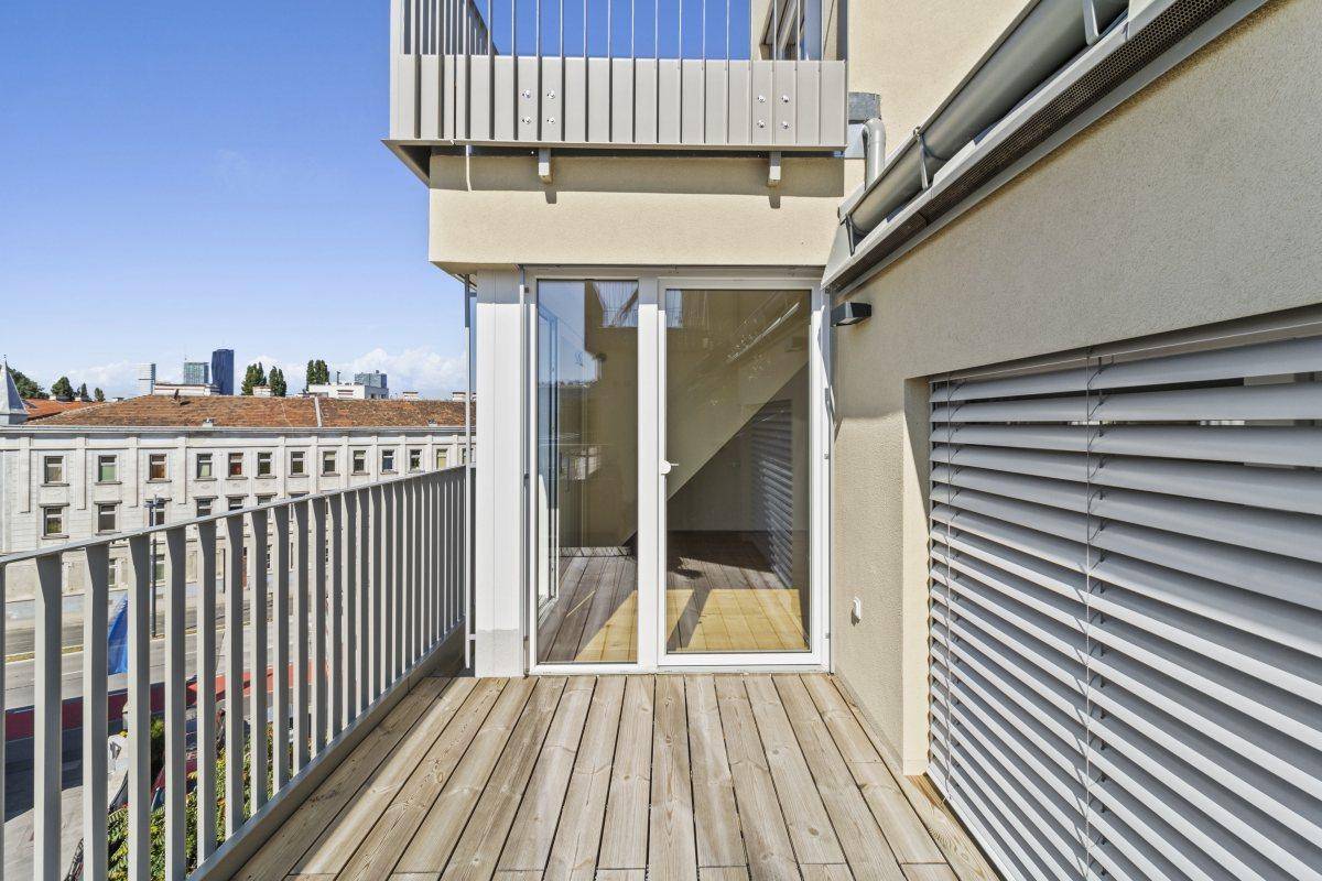 Balkon mit Holzdielen und Zugang zum Innenraum, bietet einen Blick auf die Umgebung.