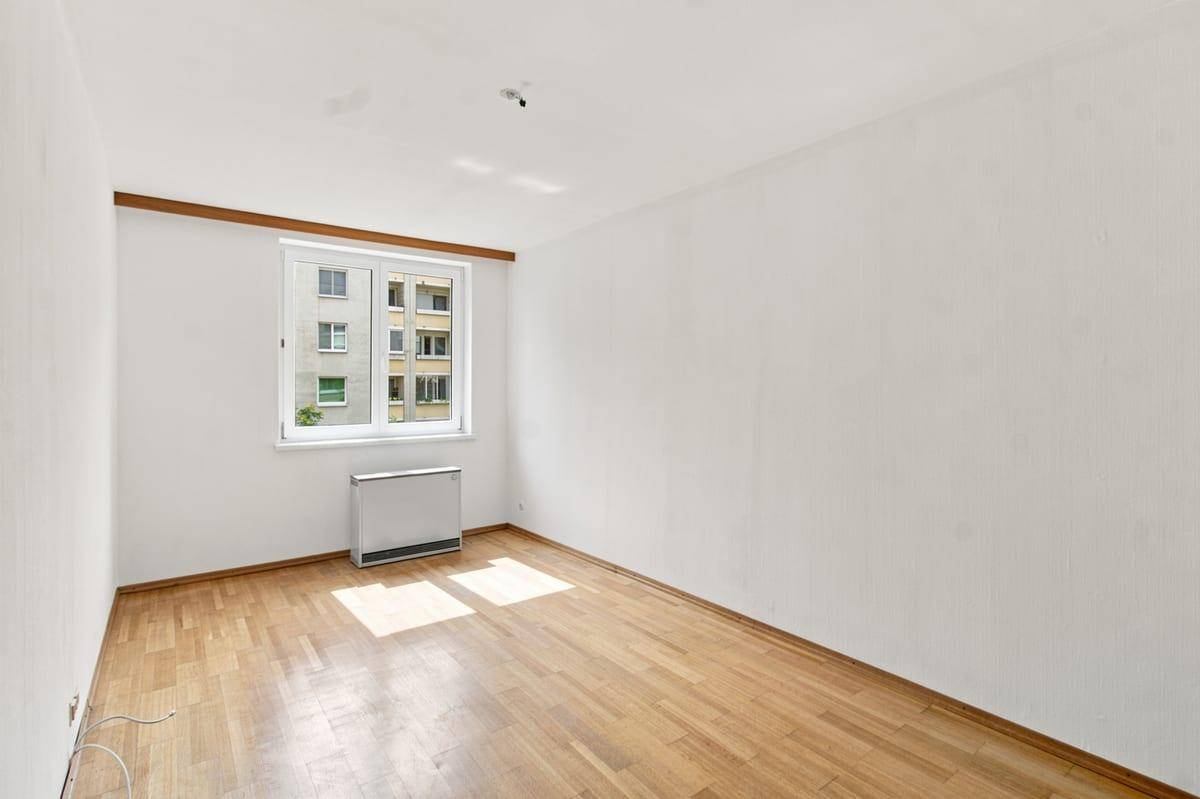Helles Schlafzimmer mit Holzboden und großem Fenster, das viel Tageslicht hereinlässt.
