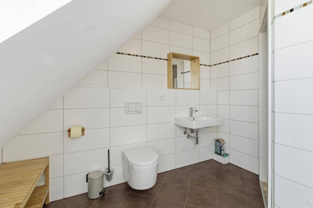 Helles Badezimmer mit weißen Fliesen, wandhängendem WC und einem Waschbecken.