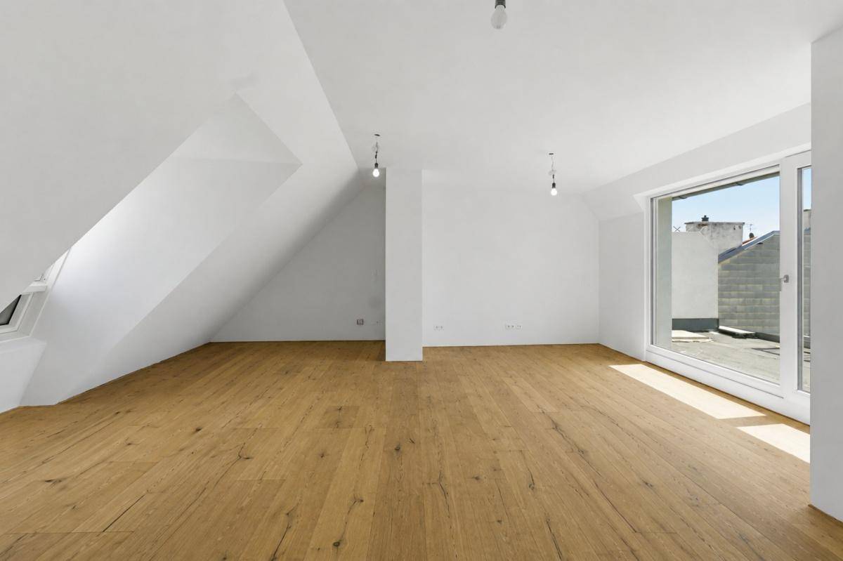 Heller, leerer Raum im Dachgeschoss mit Holzboden, weißen Wänden und Zugang zu einem Außenbereich.