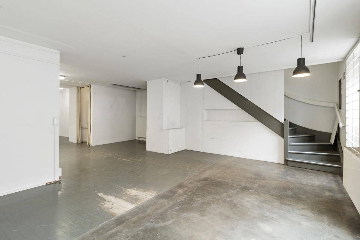 Großer, leerer Gewerberaum mit grau gestrichenem Holzboden und einer Treppe, die in einen anderen Bereich führt.