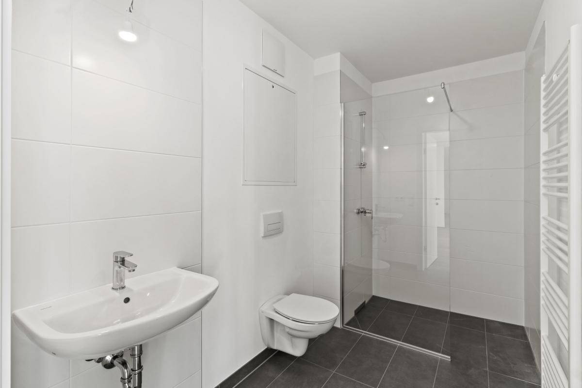 Modernes Badezimmer mit weißen Fliesen, Dusche, WC und Einzelwaschbecken.
