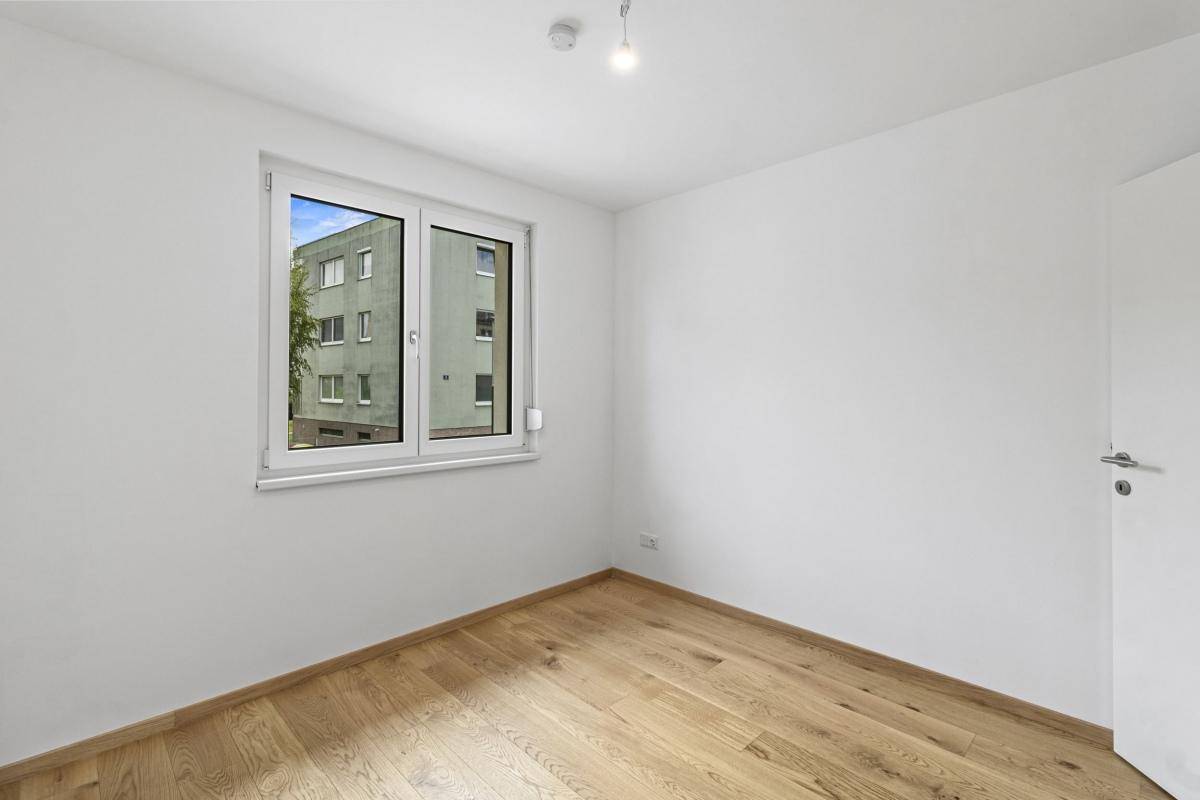 Schlafzimmer mit hellem Parkettboden und Fenster, das viel Tageslicht hereinlässt.