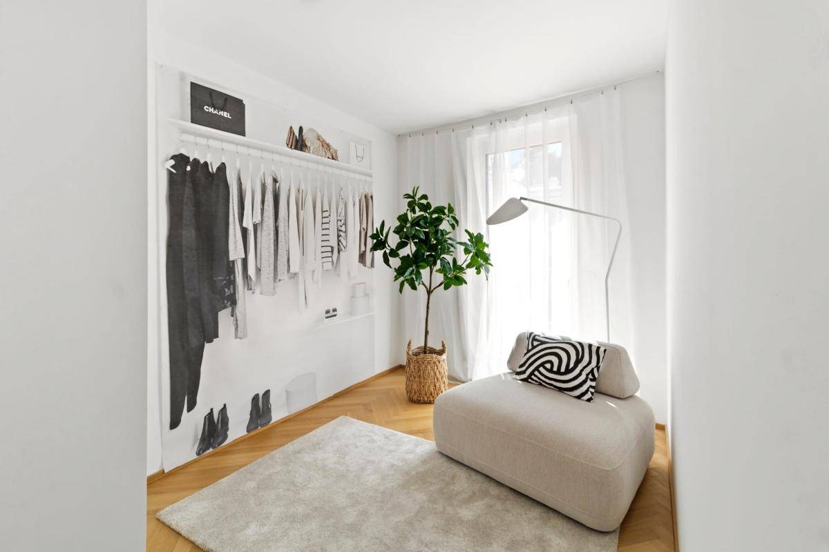 Helles Zimmer mit modernem Teppich, Sitzgelegenheit und dekorativer Kleiderstange an der Wand.