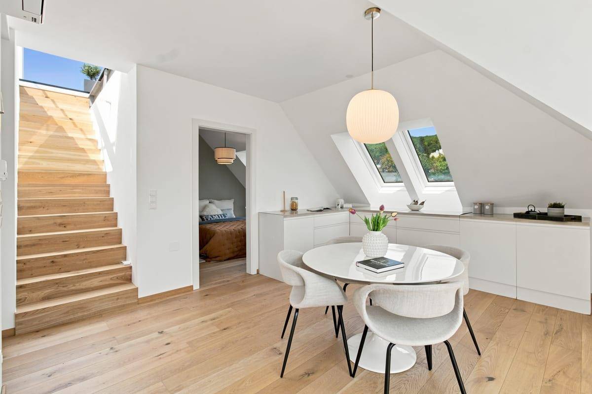 Essbereich mit modernem Tisch, Dachfenstern und Holztreppe zur Dachterrasse.