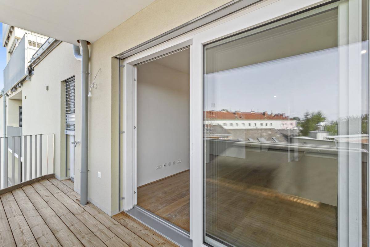 Balkon mit Holzdielen und großer Glasschiebetür, die Zugang zum Innenbereich bietet.