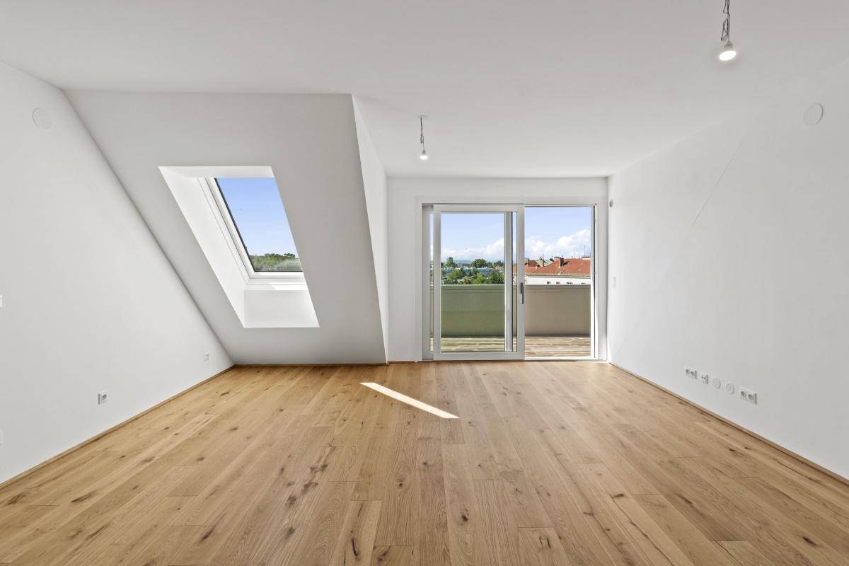 Lichtdurchfluteter Raum mit Holzboden, großem Dachfenster und Schiebetür zum Balkon.