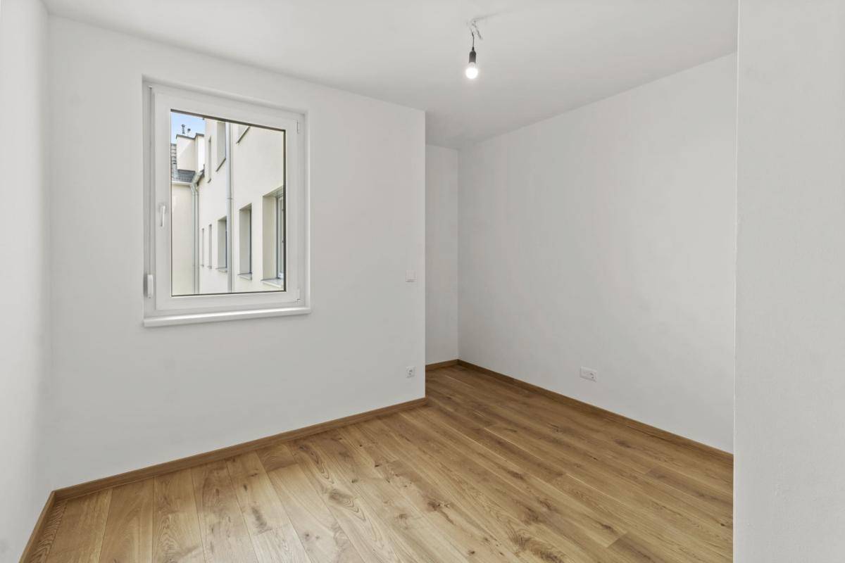 Helles Schlafzimmer mit Parkettboden und Fenster zum ruhigen Innenhof.