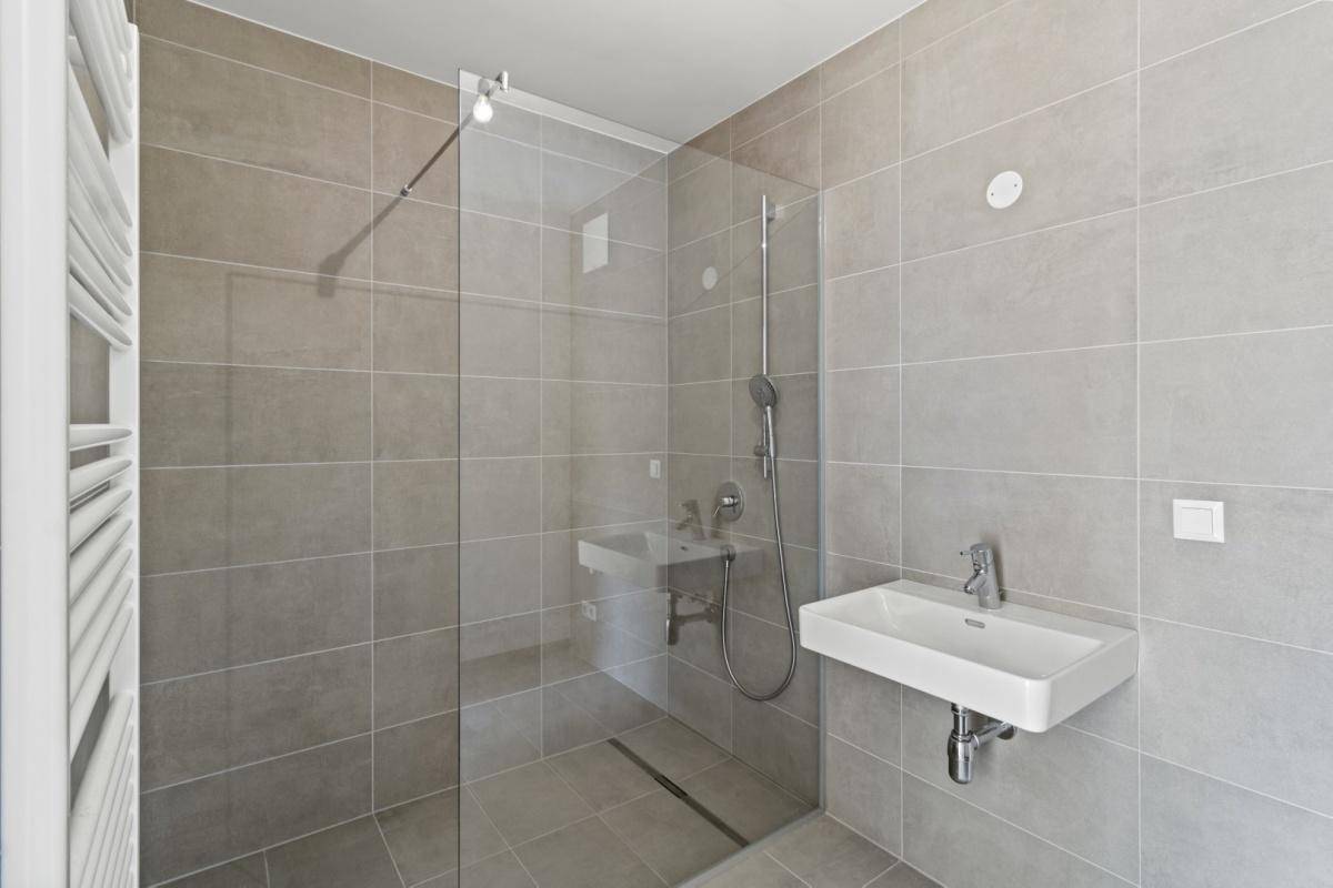 Modernes Badezimmer mit ebenerdiger Dusche, grauen Fliesen und Handtuchheizkörper.