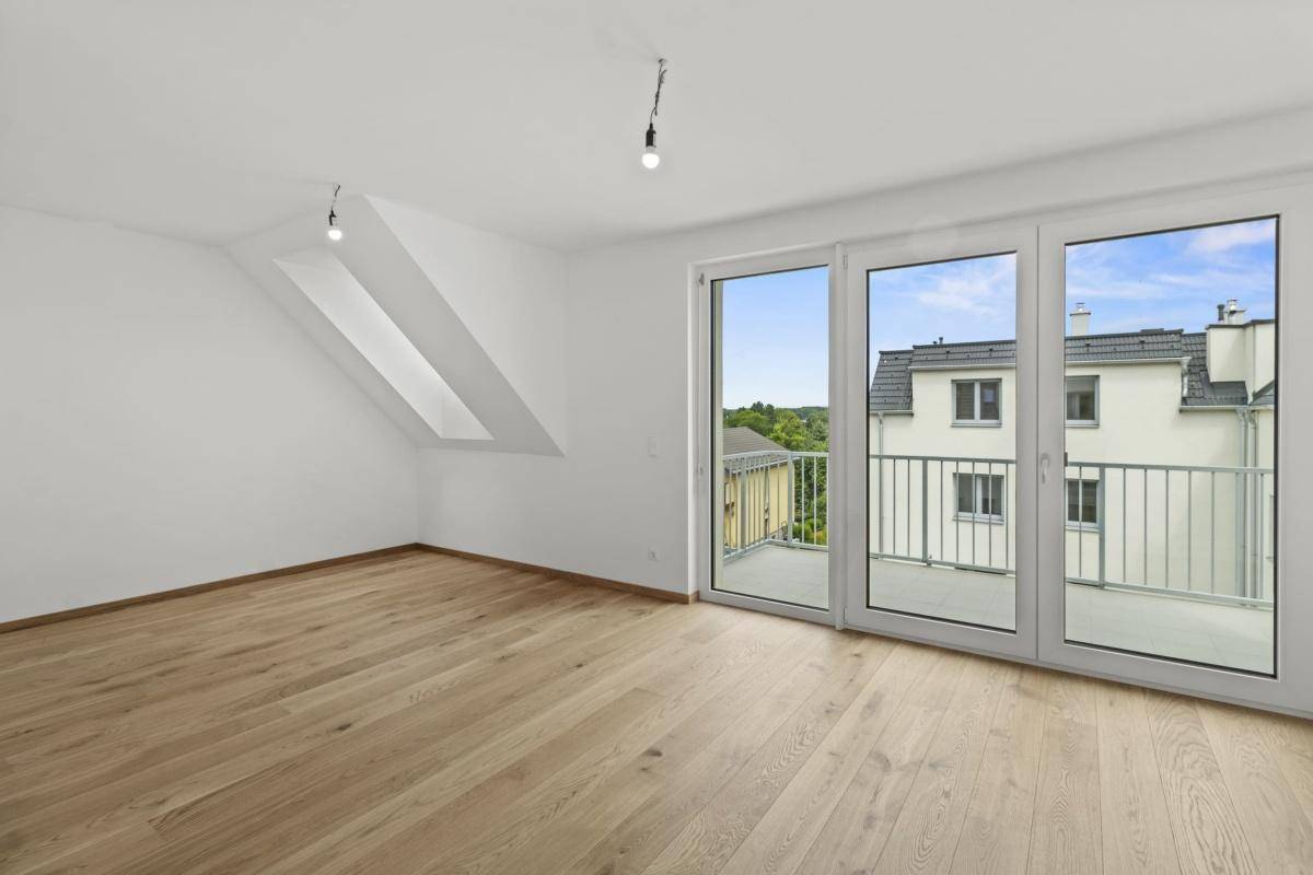 Helles Wohnzimmer mit Holzboden, Dachschräge und Zugang zu einem Balkon mit schöner Aussicht.
