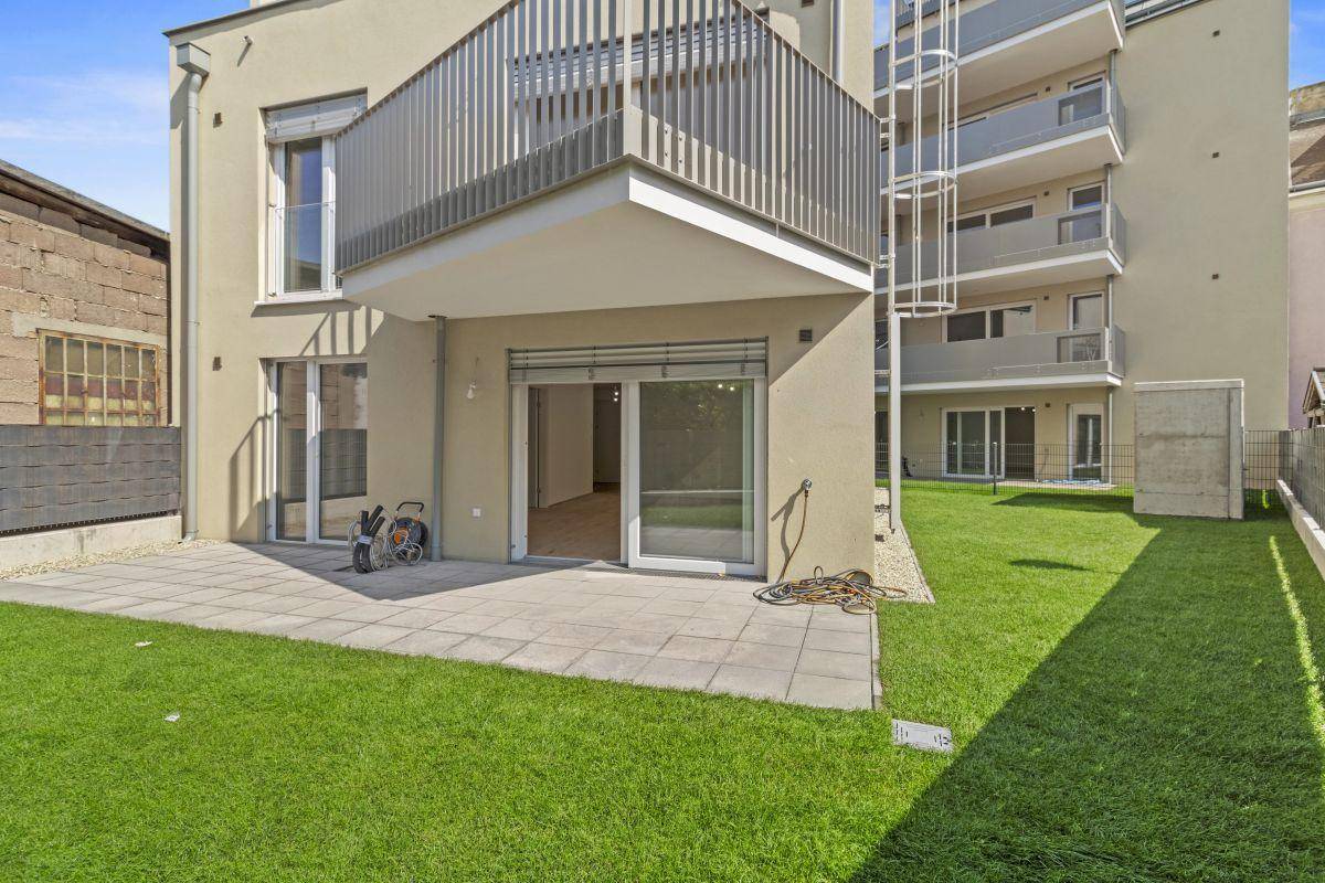 Gepflasterte Terrasse und Rasenfläche im Erdgeschoss mit Zugang zu den Wohnräumen des Neubaus.