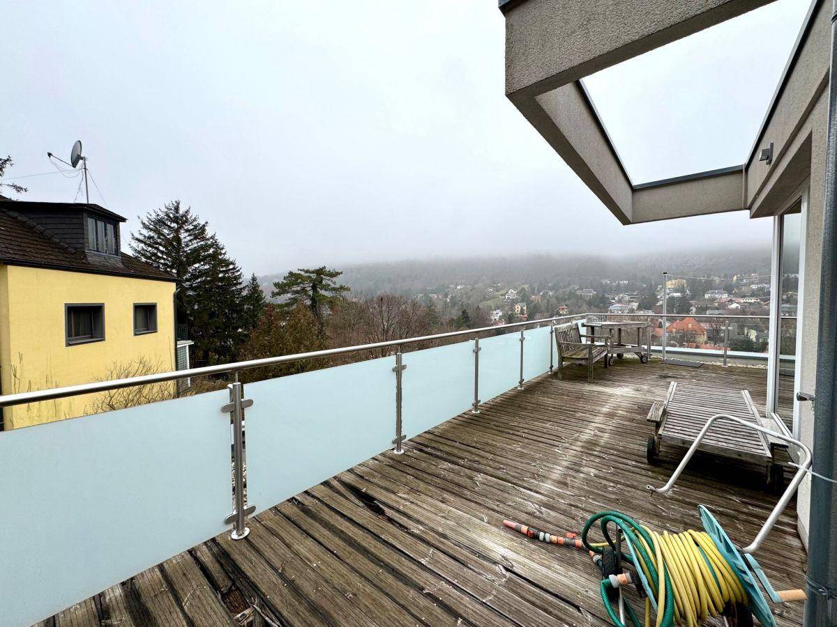 Geräumige Holzterrasse mit Glasgeländer und Gartenmöbeln, bietet einen weiten Blick über die Landschaft.