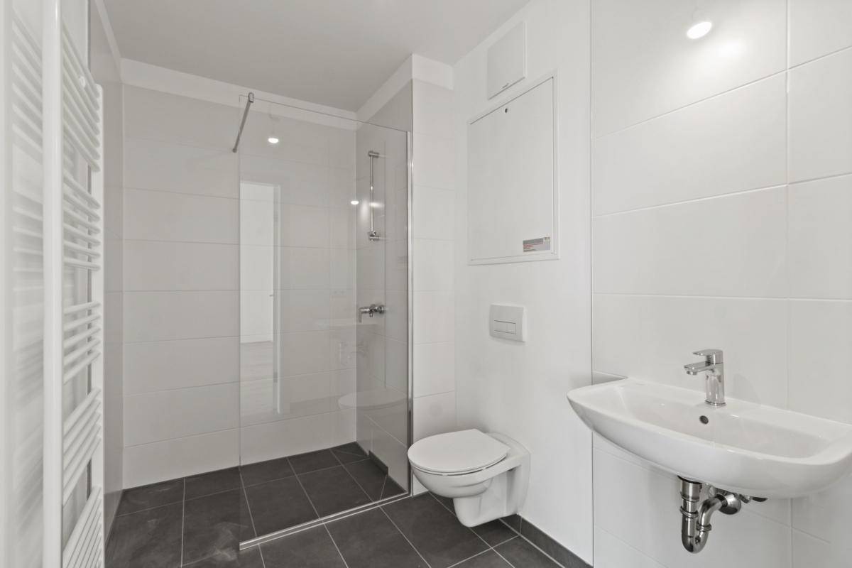 Modernes Badezimmer mit ebenerdiger Dusche, WC, Waschbecken und Handtuchheizkörper.