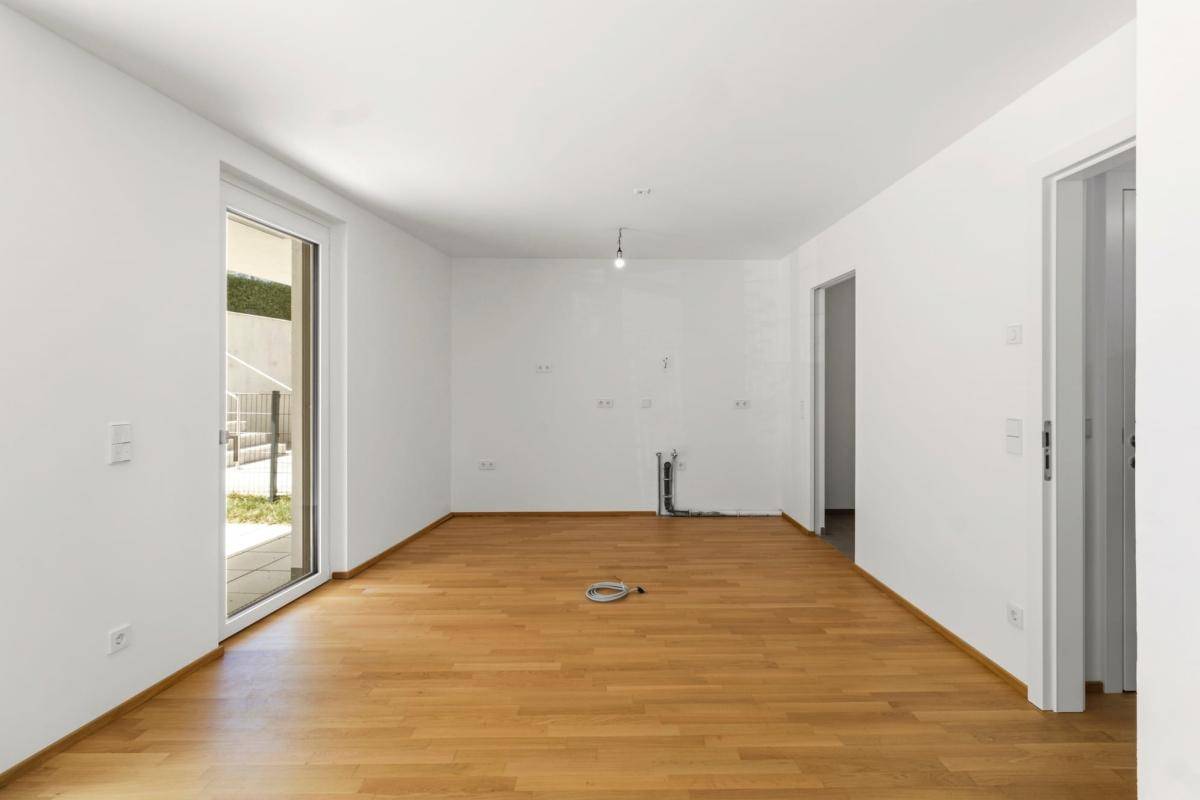 Unmöblierte Küche mit vorbereiteten Anschlüssen und direktem Zugang zum Außenbereich.