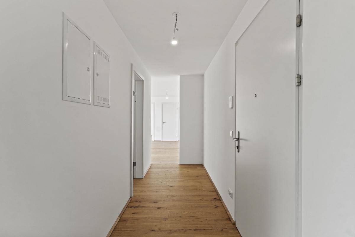 Langer, heller Flur mit Holzboden und weißen Wänden, der zu weiteren Räumen führt.