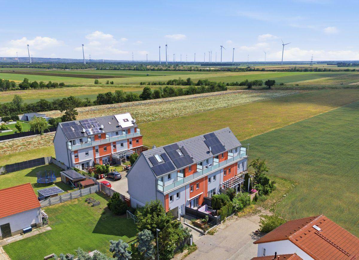 Weitläufige Luftaufnahme von zwei Reihenhausblöcken mit Photovoltaik und angrenzenden Feldern.