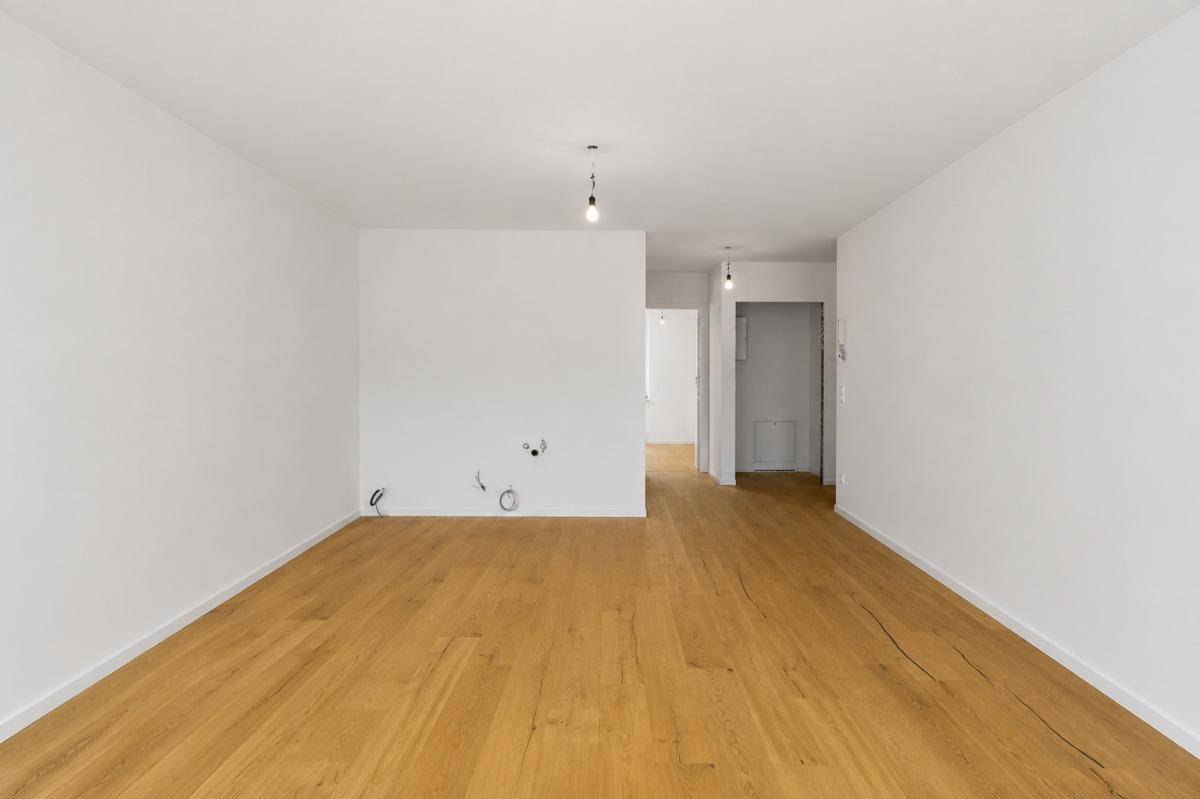 Geräumiger Raum mit Holzboden und weiß gestrichenen Wänden, offen zum Flurbereich.