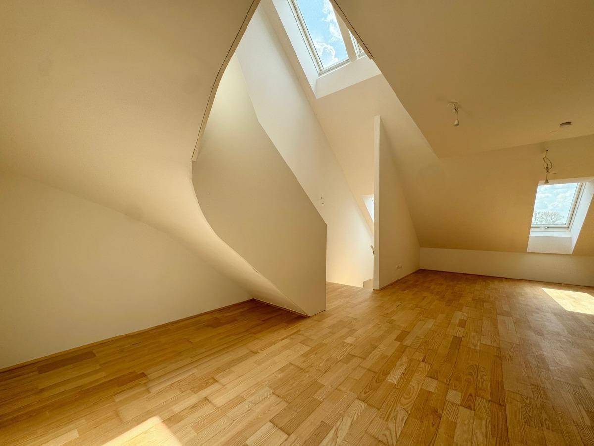 Geräumiger Dachgeschossraum mit Holzboden, hohen Decken und architektonischen Elementen.