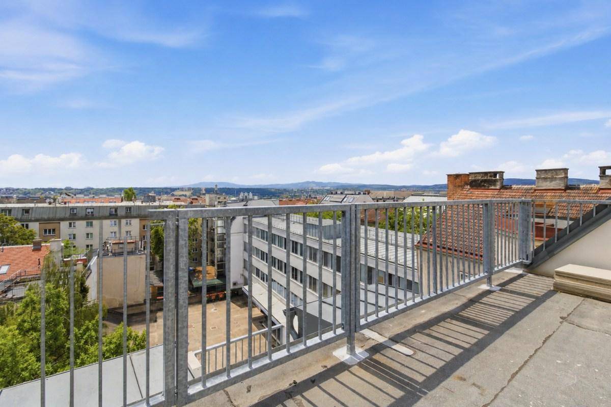 Unmöblierte Dachterrasse mit Metallgeländer und Panoramablick über die städtische Umgebung.