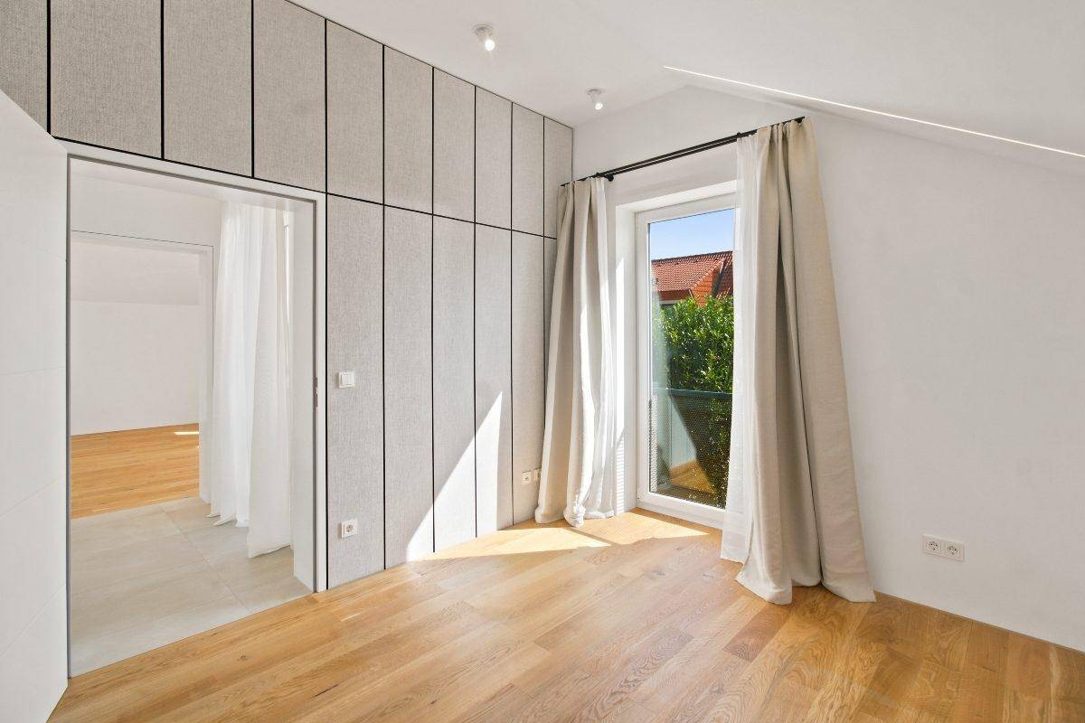 Helles Schlafzimmer mit Holzboden und integrierten Kleiderschränken, bietet Zugang zu einem Balkon.