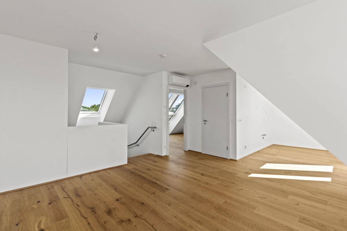 Geräumiger Dachgeschossraum mit Holzboden, Dachschrägen und mehreren Dachfenstern.