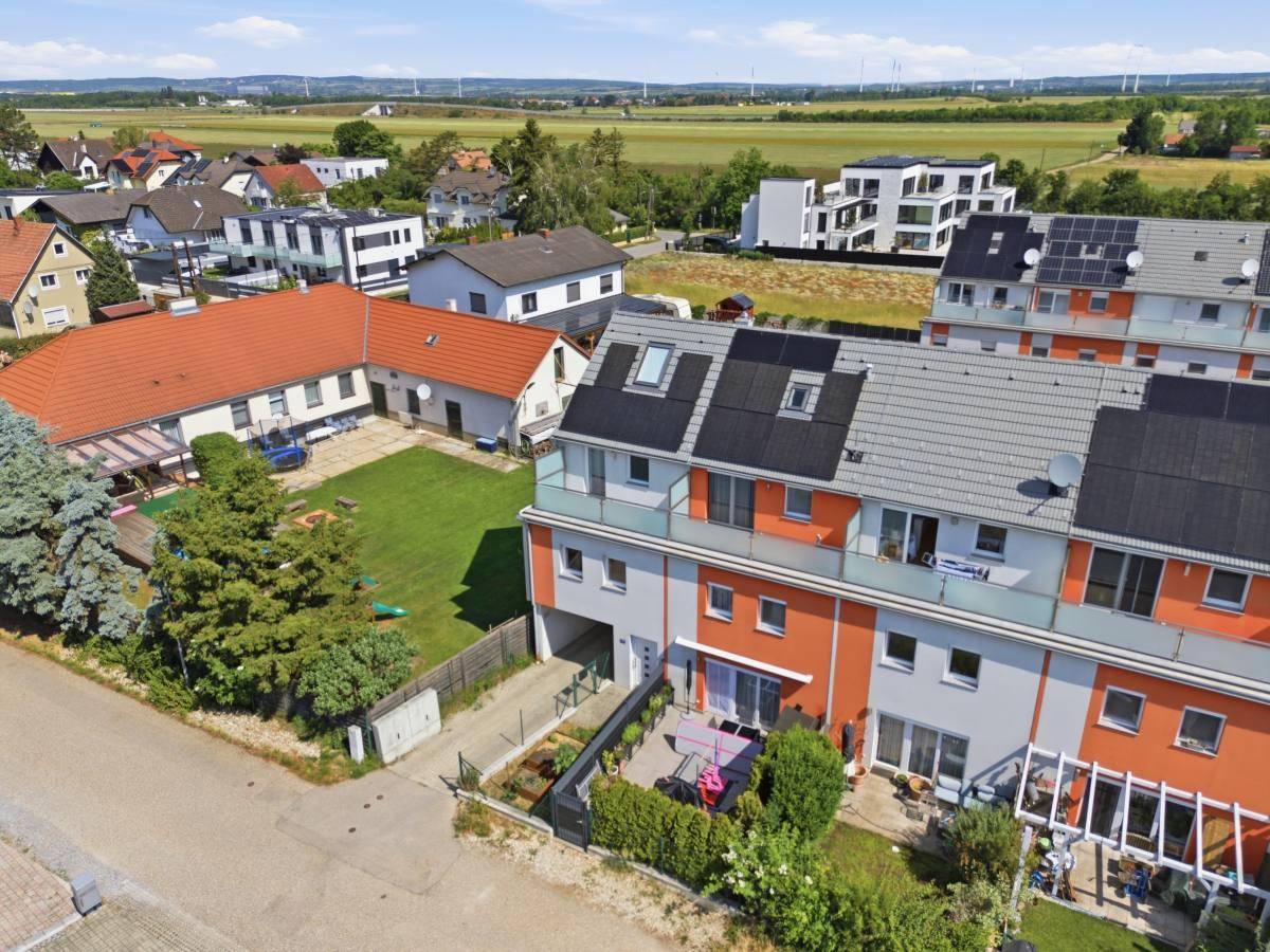 Luftaufnahme der Reihenhäuser mit Gärten und Terrassen, angrenzend an grüne Felder und weitere Wohnhäuser.