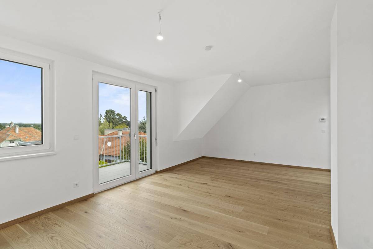 Heller, leerer Raum mit Holzboden, weiß gestrichenen Wänden und Zugang zum Balkon.