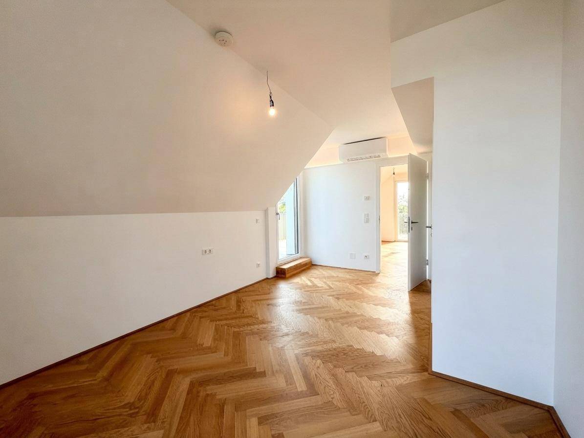 Helles Zimmer im Dachgeschoss mit Schrägdecke, Parkettboden und Zugang zu einem Balkon.