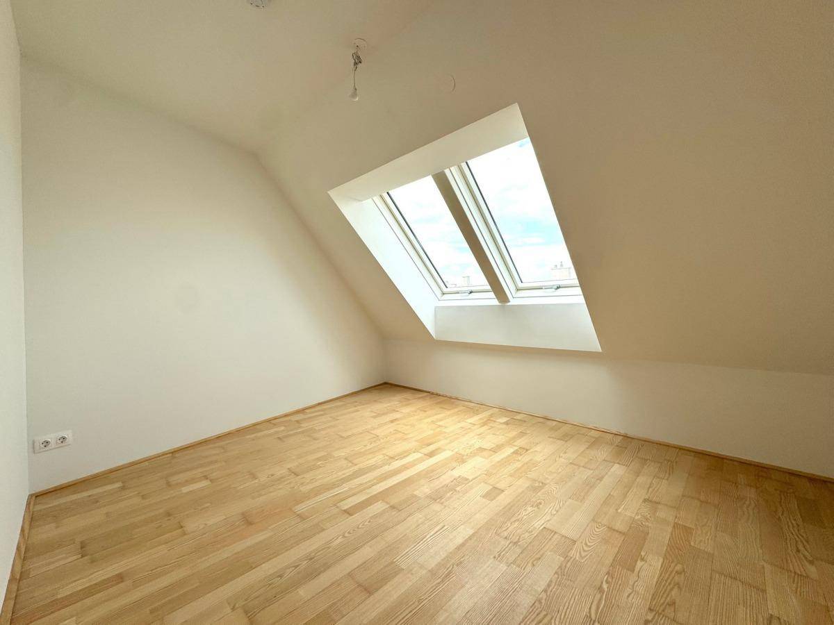 Heller Dachgeschossraum mit Holzboden und großen Dachfenstern, die viel Licht hereinlassen.