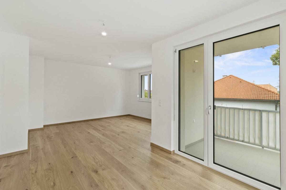 Heller, leerer Raum mit Eichenparkettboden und Zugang zu einem Balkon, frisch gestrichen.