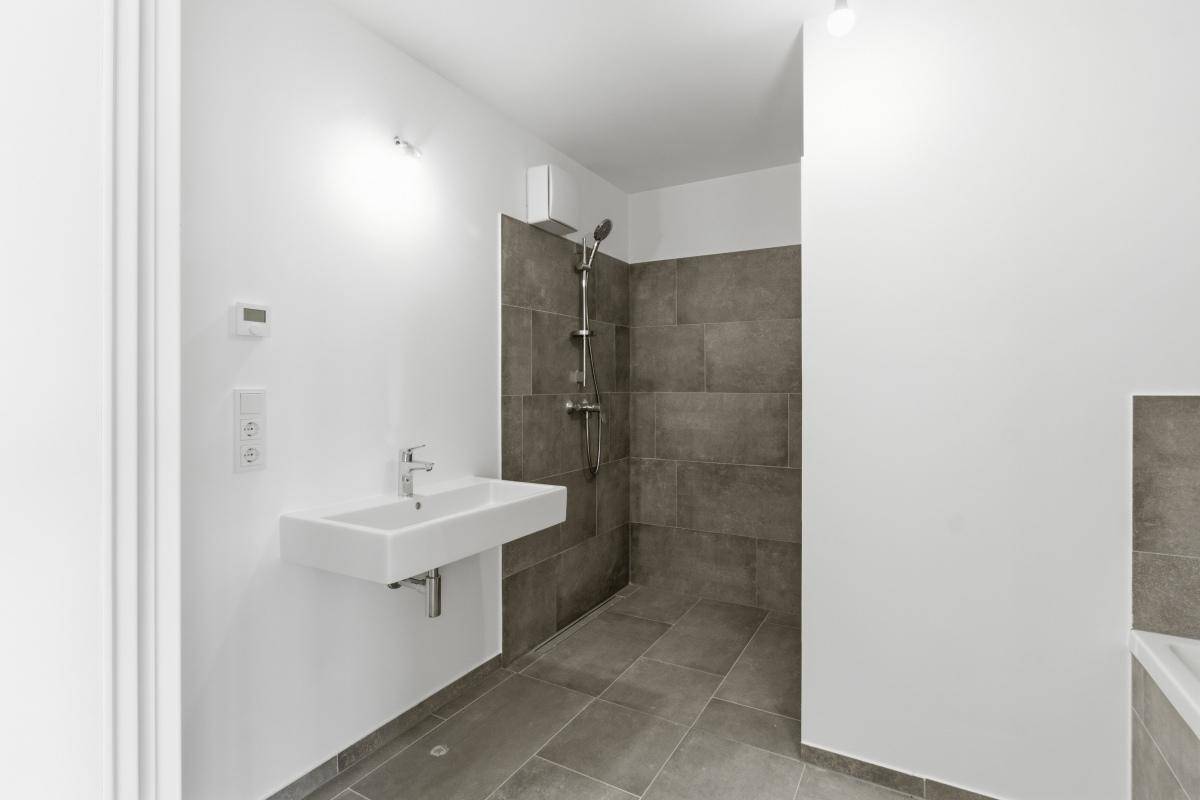Helles Badezimmer mit Duschbereich und modernem Waschbecken, in zeitlosem Grau gefliest.
